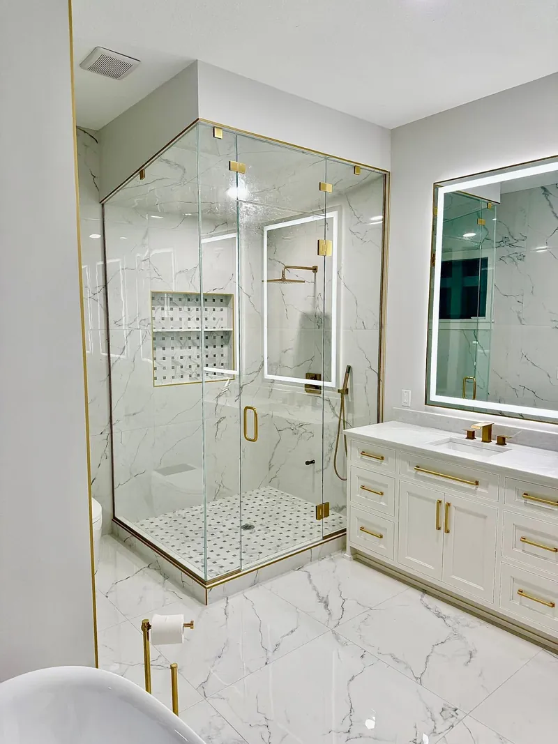 Frameless glass shower with gold hardware in a marble bathroom